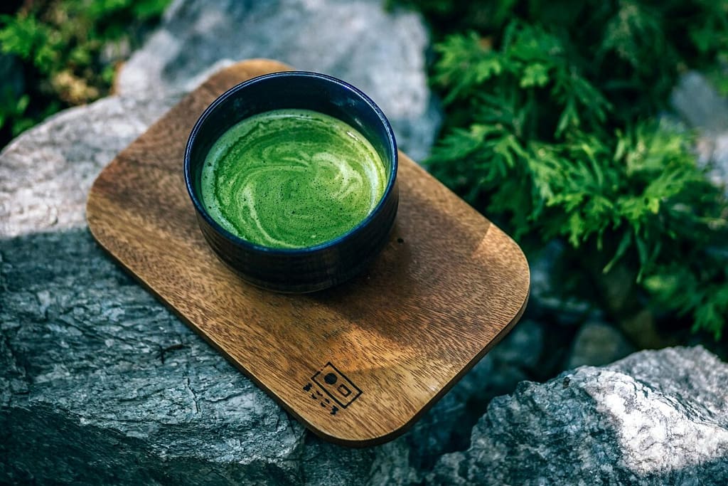 Green Tea in a black cup on arock in a forest
